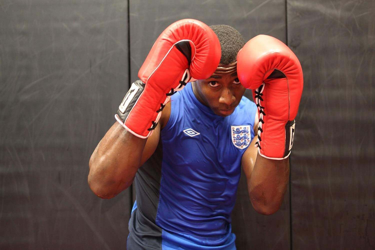 Boxer in a defensive guard stance wearing red boxing gloves.