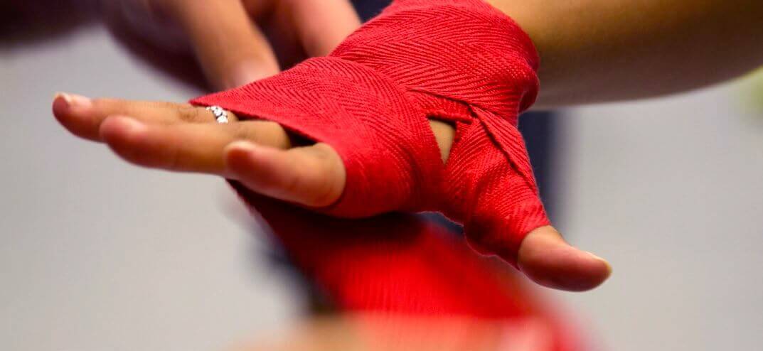 Boxer wrapping hands with red hand wraps before putting on gloves.
