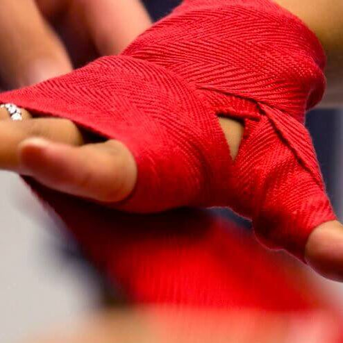 Boxer wrapping hands with red hand wraps before putting on gloves.
