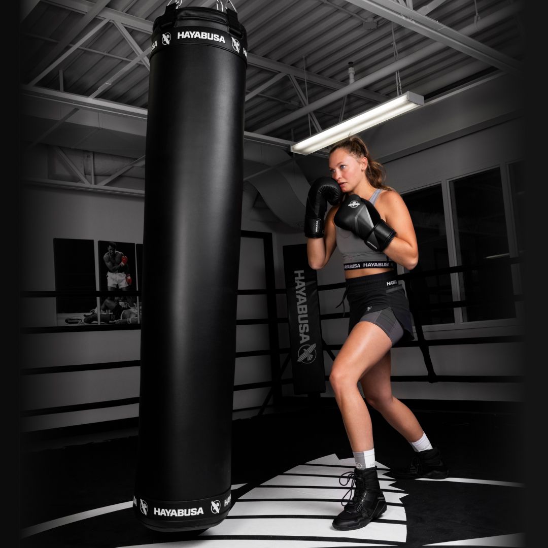 Person in boxing attire standing next to a punching bag in a gym setting