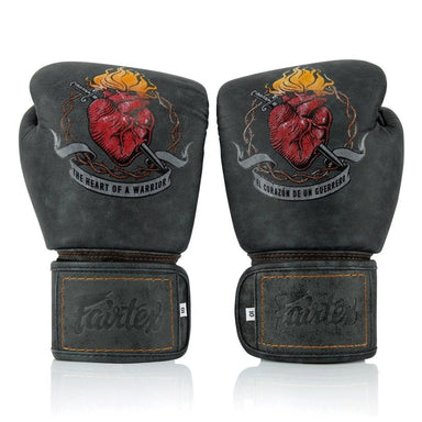 A pair of black leather boxing gloves with a red anatomical heart graphic and a dagger, featuring the Fairtex logo on the wrist straps, set against a plain white background.