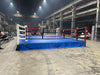 Boxing ring with blue mat and red ropes in an industrial setting