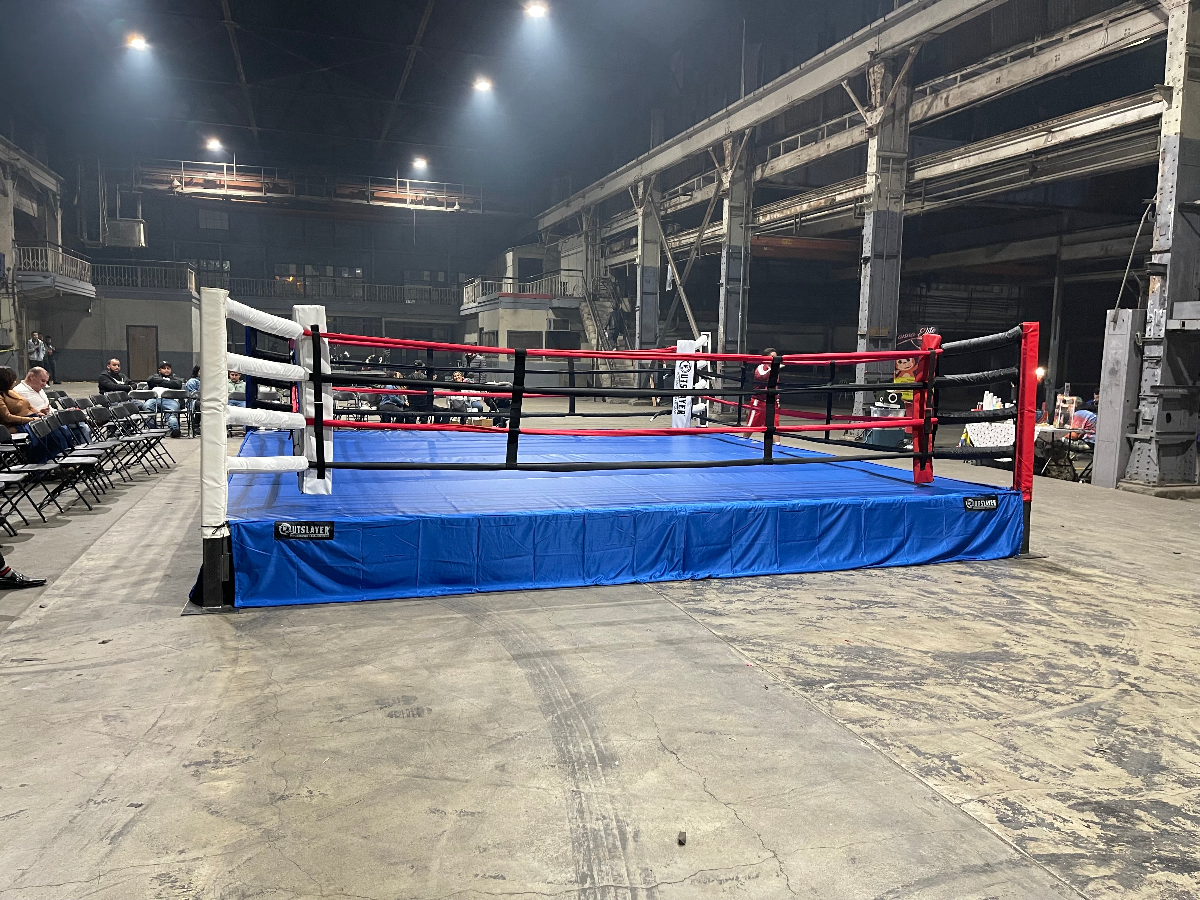 Boxing ring with blue mat and red ropes in an industrial setting