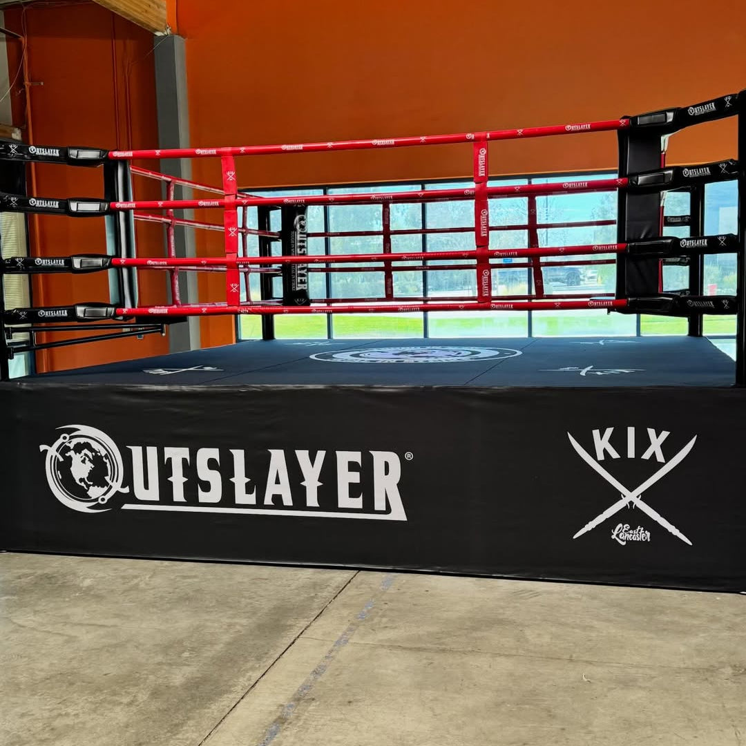 Boxing ring with 'Outslayer' and 'Kix' branding in an indoor setting.